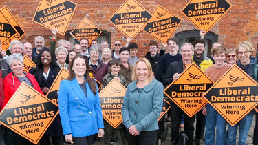 crowd of supporters behind Liberal Democrat MPs holding up supportive signs