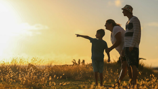 A child and two adults look at a sunset